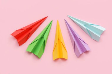 Pembe arka planda renkli kağıt uçaklar