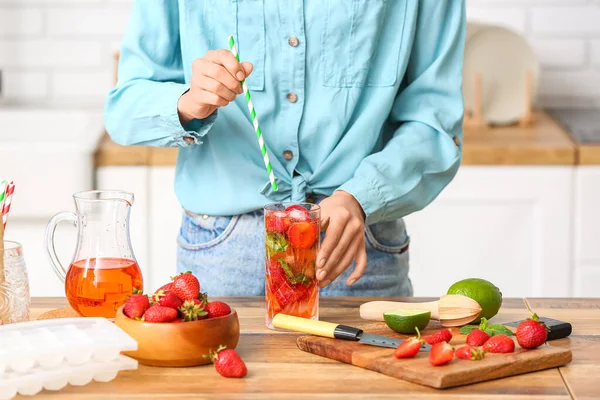 Woman with glass of cold strawberry lemonade in kitchen