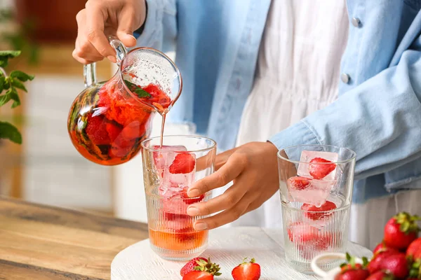 Woman pouring tasty strawberry lemonade into glass in kitchen, closeup