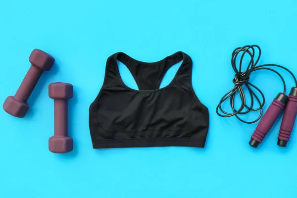 Dumbbells, skipping rope and sports bra on color background