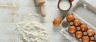 Taze yumurtalı buğday unu, bir sürahi süt ve beyaz ahşap arka planda merdane.