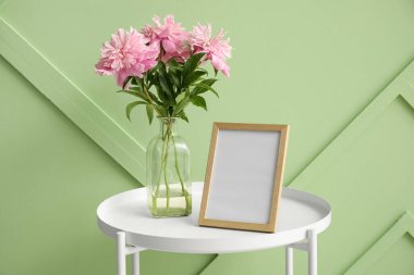 Boş fotoğraf çerçevesi ve vazo ile yeşil duvarın yanında güzel şakayık çiçekleri.