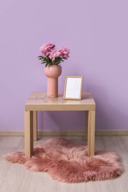 Vazo dolusu şakayık çiçeği, boş fotoğraf çerçevesi ve odanın duvarının yanındaki masada kadın aksesuarları.