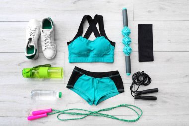 Female sportswear and different equipment for pilates on light wooden background