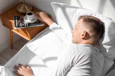 Yakışıklı genç adam yatak odasındaki masadan kahve alıyor.