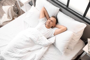 Handsome young man lying in bed at home