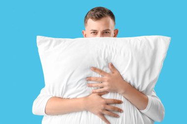 Young man with pillow on blue background