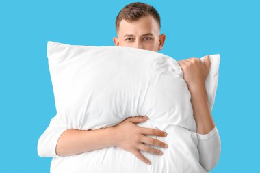 Young man with pillow on blue background