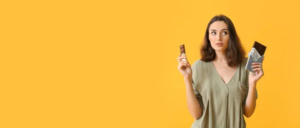 Sarı Arka Planda Lezzetli Çikolataları Olan Düşünceli Genç Bir Kadın — Stok fotoğraf
