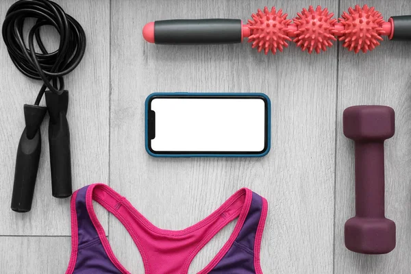 Mobile phone, female top and sports equipment on grey wooden background