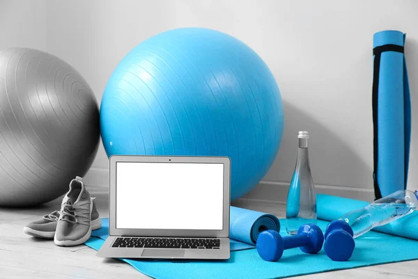 Modern laptop and sports equipment on floor near white wall