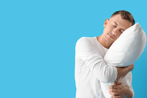 Sleepy young man with pillow on blue background