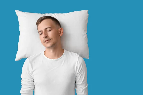 Young man with pillow sleeping on blue background