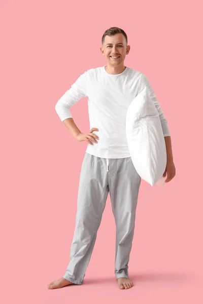 Young man with pillow smiling on pink background