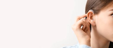 Young woman with hearing aid on light background, closeup. Banner for design 