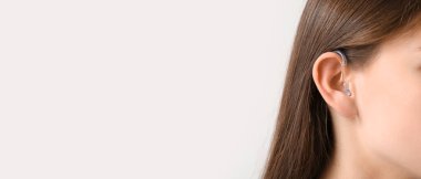 Young woman with hearing aid on light background, closeup. Banner for design 