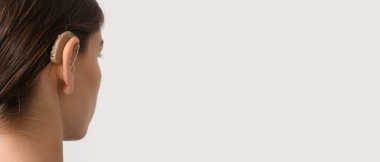 Young woman with hearing aid on light background. Banner for design 