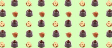 Many tasty chocolate candies and nuts on green background. Pattern for design