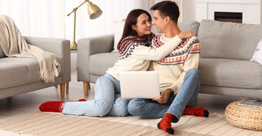 Evde dizüstü bilgisayar kullanan, sıcak kazaklı mutlu bir çift.