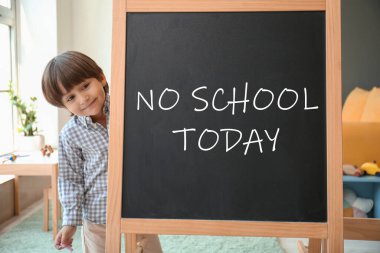Cute little boy and chalkboard with written text NO SCHOOL TODAY in classroom