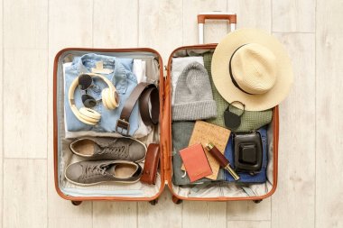 Beyaz ahşap arka planda seyahat etmek için erkek aksesuarlarıyla dolu bavul.