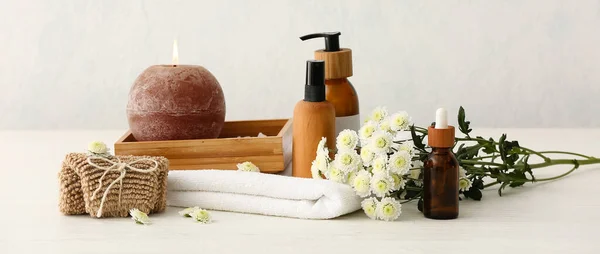 Set of bath supplies, candle and flowers on light background