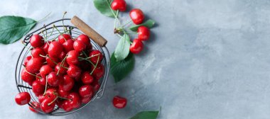Basket of tasty cherries on light blue background with space for text, top view