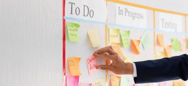 Businessman attaching sticky note to scrum task board in office, closeup
