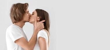 Kissing young couple on light background with space for text