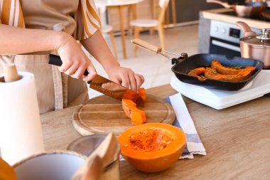 Young woman cutting pumpkin in kitchen, closeup