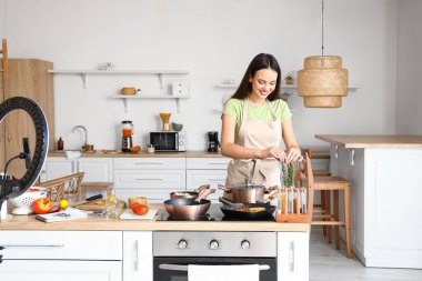 Young woman taking rosemary while recording video tutorial in kitchen