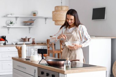 Young woman making dough for pancakes while following video tutorial in kitchen