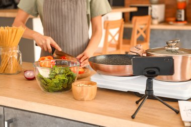 Young woman cutting onion while following video tutorial in kitchen, closeup
