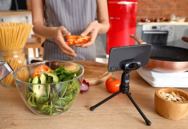 Stand with mobile phone, bowl and vegetable salad on table in kitchen, closeup