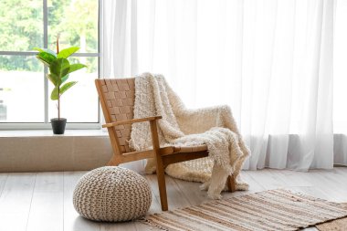 Cozy armchair with plaid and pouf near window