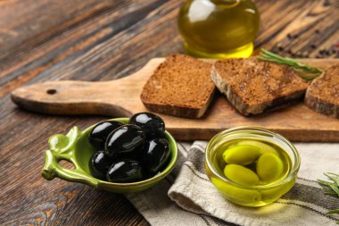 Bowls of olives and oil on wooden table, closeup