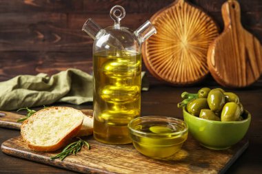 Board with bottle of fresh oil, bread and olives on dark wooden background