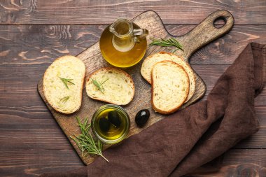 Board with slices of fresh bread and olive oil on wooden background