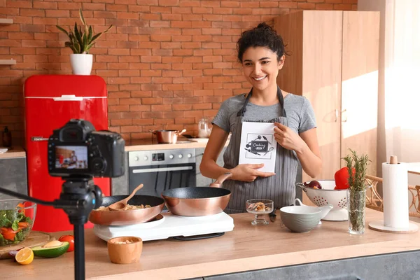 Young woman with cooking book recording video class in kitchen