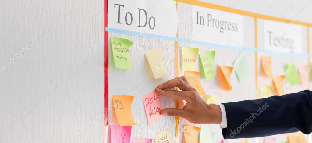 Businessman attaching sticky note to scrum task board in office, closeup