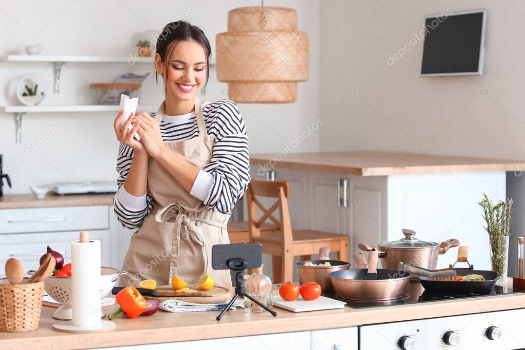 Young woman wiping her hands with paper towel while watching cooking video tutorial in kitchen