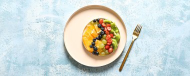 Plate of tasty fruit salad on light blue background, top view
