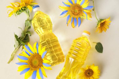 Bottles of oil and sunflowers in colors of Ukrainian flag on light background