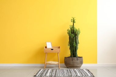 Big cactus and table with frame near yellow wall