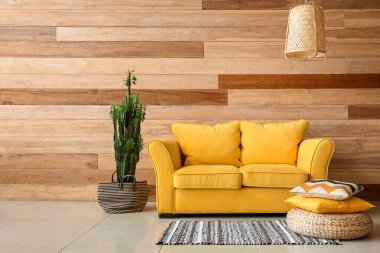 Big cactus, yellow sofa, pouf and pillows near wooden wall