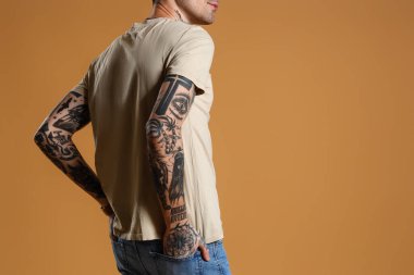 Young tattooed man in beige t-shirt on brown background