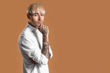Young tattooed man in white sweater on brown background