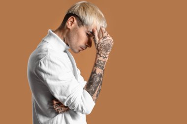 Young tattooed man in white sweater on brown background