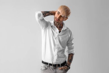 Young tattooed man in white shirt on light background