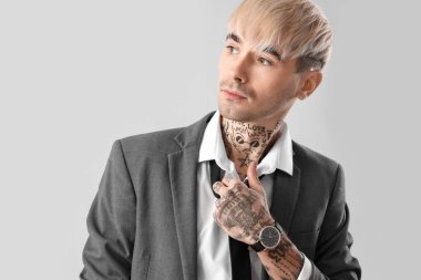Young tattooed man with necktie on light background